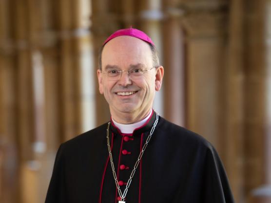 Weihbischof Brahm in festlicher Kleidung steht im Bogengang des Doms